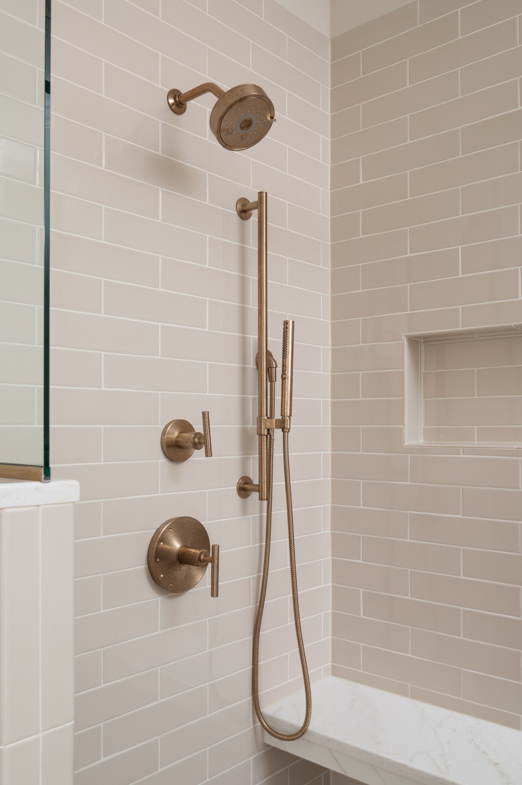Brass shower fixtures with handheld sprayer and controls in Michiana primary bathroom
