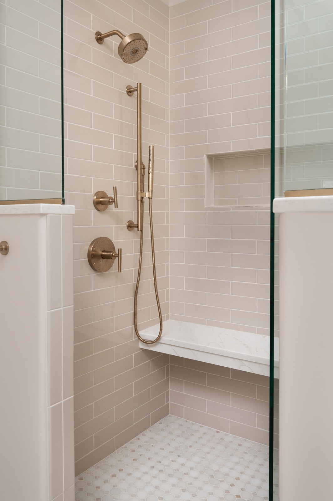 Complete shower remodel with beige subway tile, brass fixtures, and marble bench in Michiana primary bathroom, designed by Peacock and Co