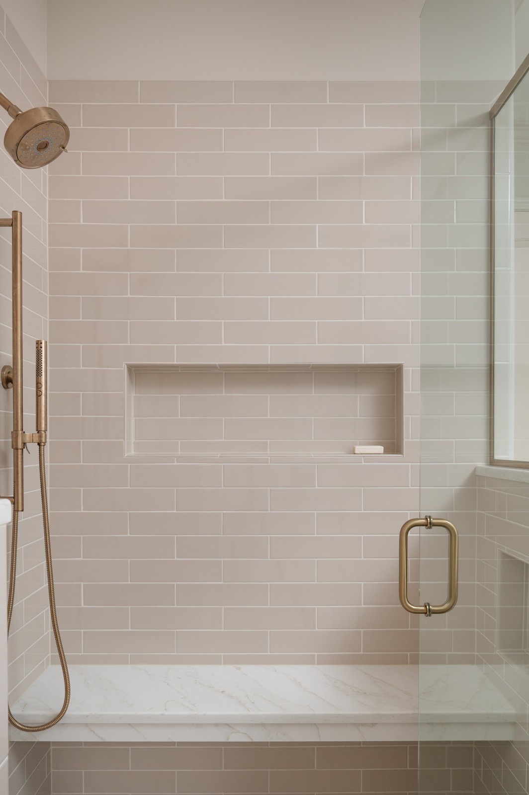 Walk in shower with beige subway tile and tiled niche in Michiana primary bathroom, designed by Peacock and Co