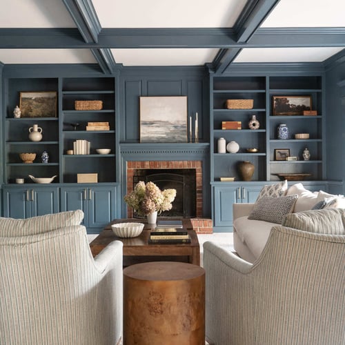 Blue living room with coffered ceiling, built-in shelves, brick fireplace, white sofa, chairs, and wood tables (1)