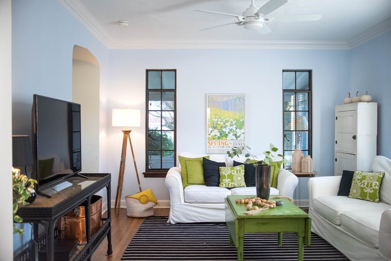 Bright living room with white sofas, green accents, wood floors, and tall windows in a stylish home located in Greater Michiana