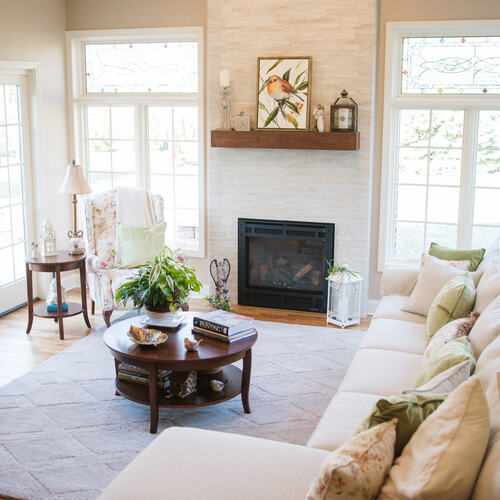 Bright sunroom with a fireplace, white sofa, floral chair, round coffee table, and large windows