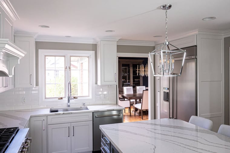 Bright white kitchen in Harbor Country featuring a large quartz island, modern chandelier, stainless steel appliances, and open view to a formal dining room
