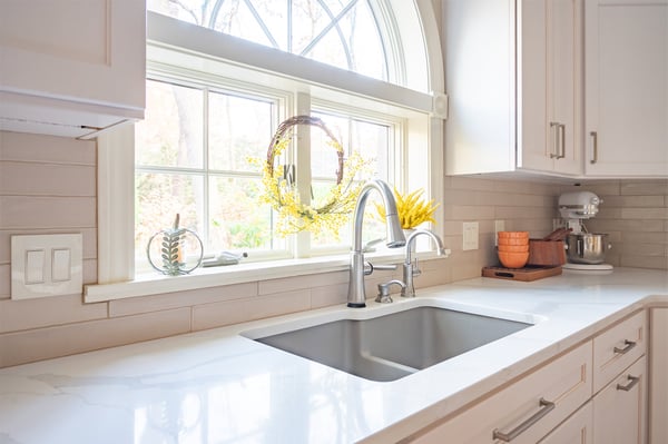Bright white kitchen sink area with beautiful fixtures, remodeled by Peacock & Co
