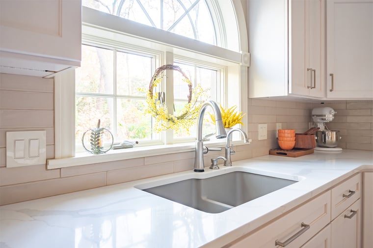 Bright white kitchen sink area with beautiful fixtures, remodeled by Peacock & Co