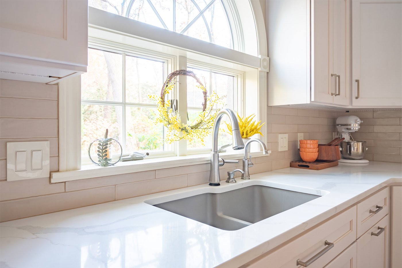 Bright white kitchen sink area with beautiful fixtures, remodeled by Peacock & Co