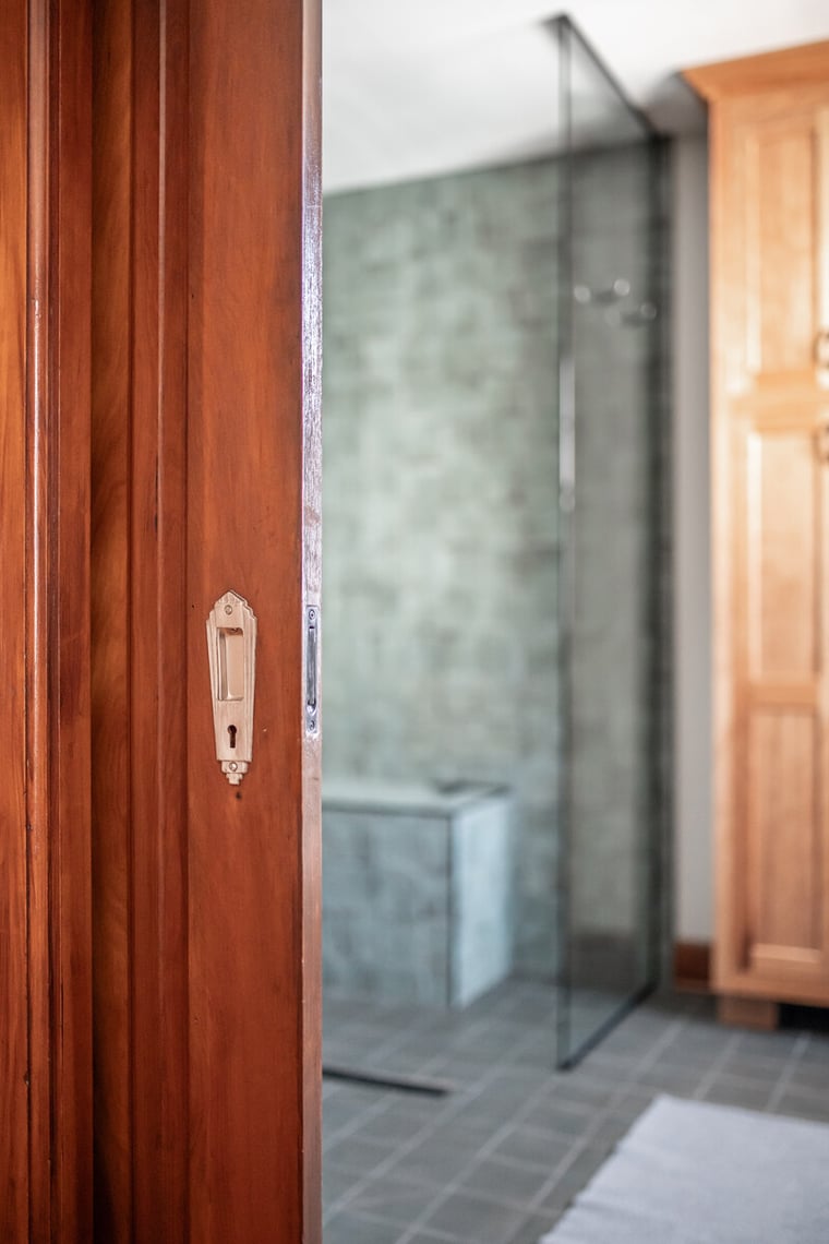 Oak pocket door with vintage hardware outside custom bathroom with green subway tiles in South Bend by Peacock and Co