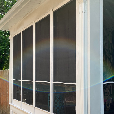 Exterior view of a screened porch with black mesh panels, white trim, and a gutter downspout