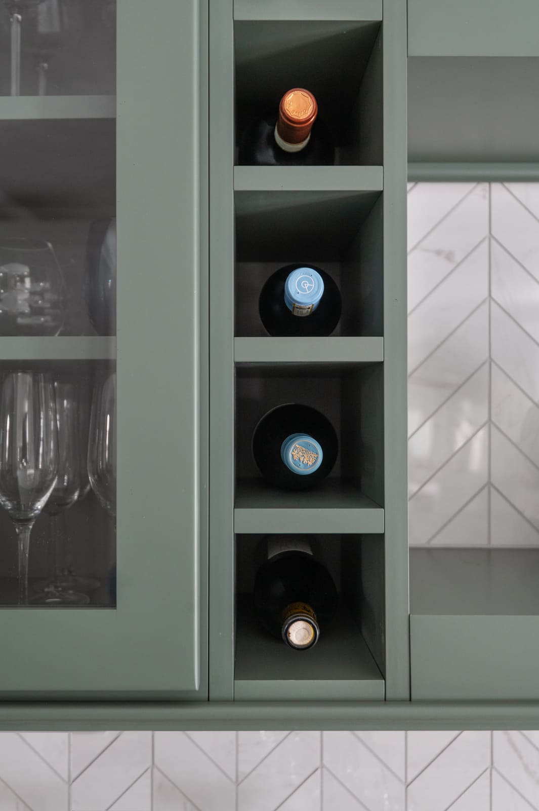Built-in wine storage beside sage green glass-front cabinets and white chevron tile in a Granger, IN kitchen