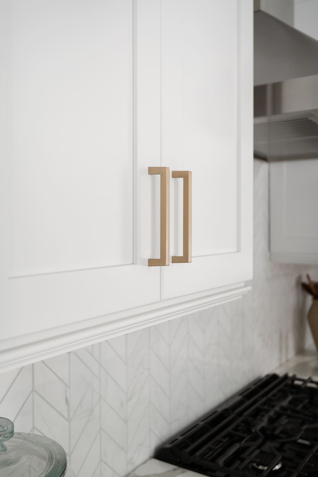 Close-up of white kitchen cabinets with brass pulls and chevron tile backsplash in a Granger, IN kitchen