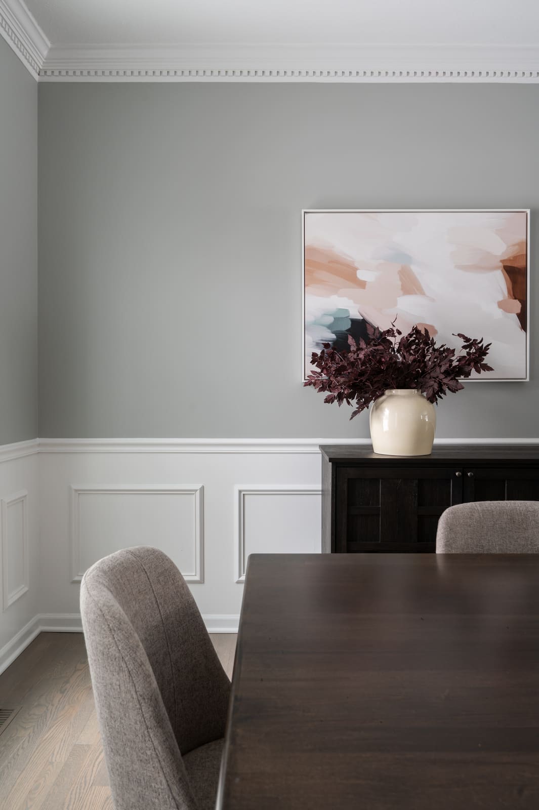 Dining room in Granger, IN with gray walls, white wainscoting, dark wood table, and abstract artwork