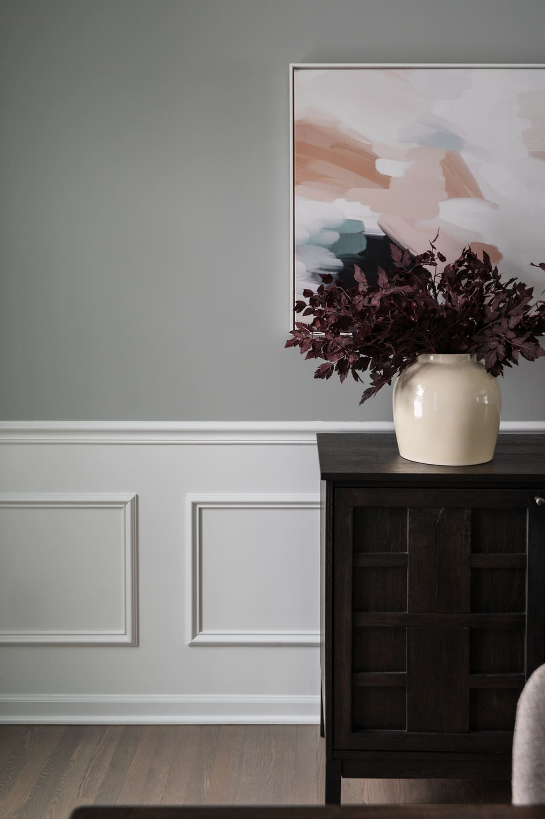 Dining room vignette in Granger, IN with gray walls, white wainscoting, abstract art, and a dark sideboard with vase