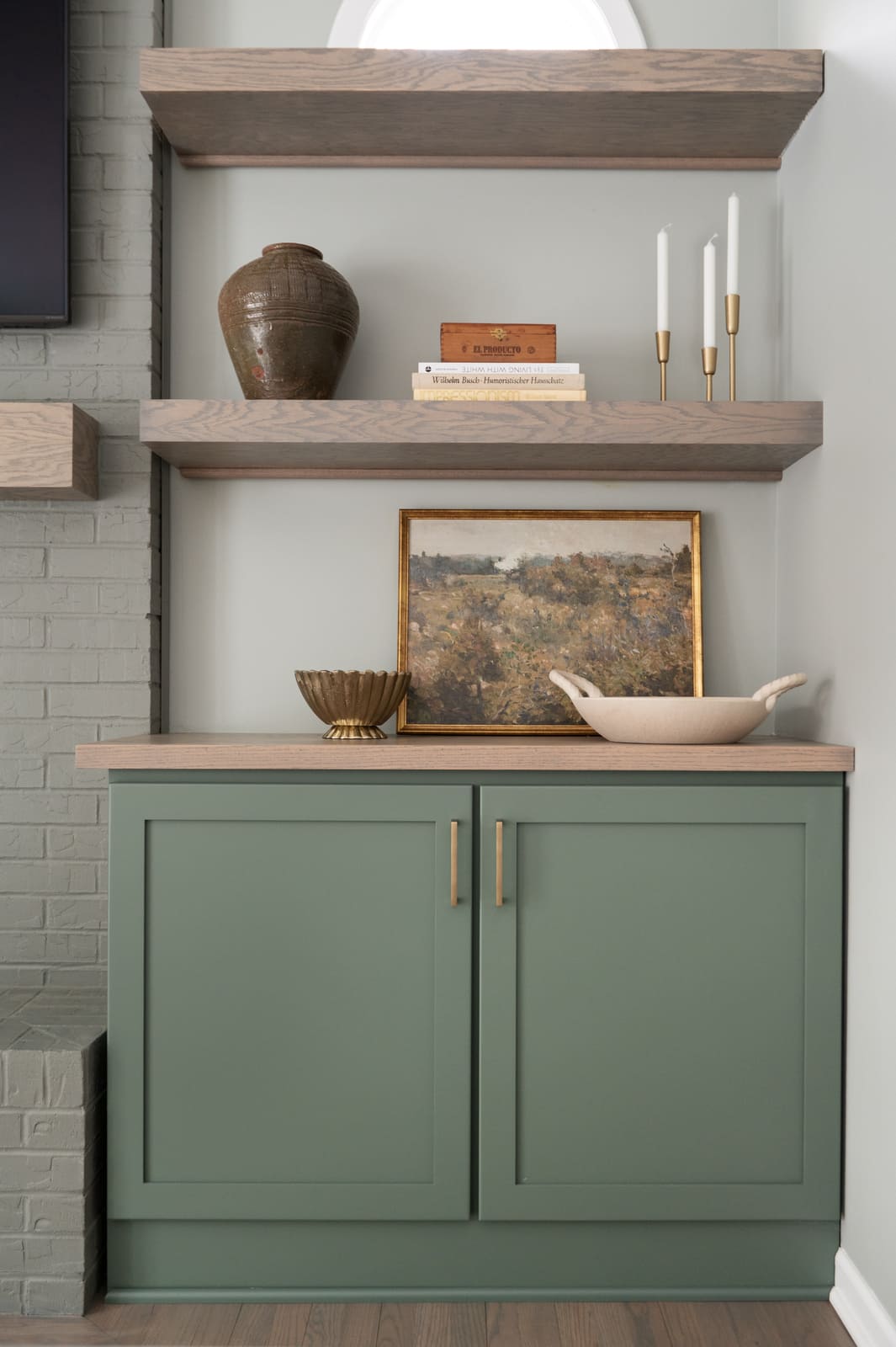 Granger, IN built-in with sage green cabinet, wood floating shelves, framed art, and brass candlesticks