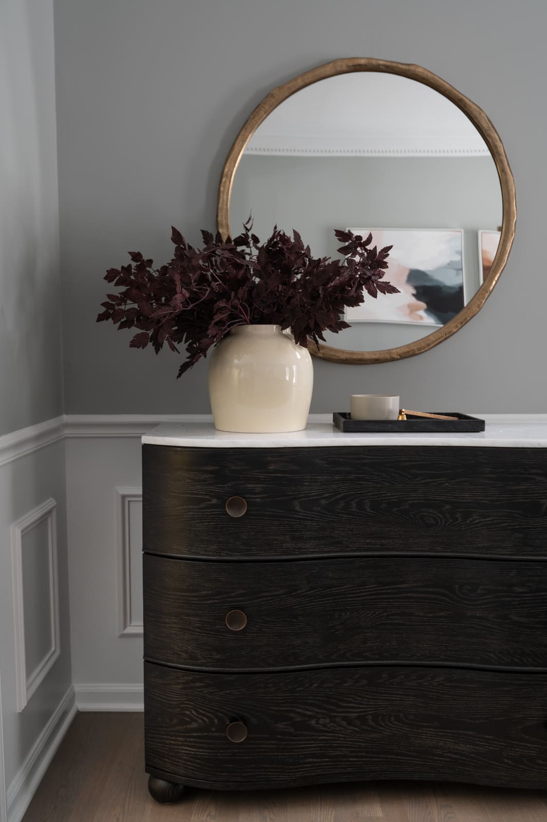 Granger, IN dining room vignette with round mirror, black console, marble top, and cream vase with burgundy branches