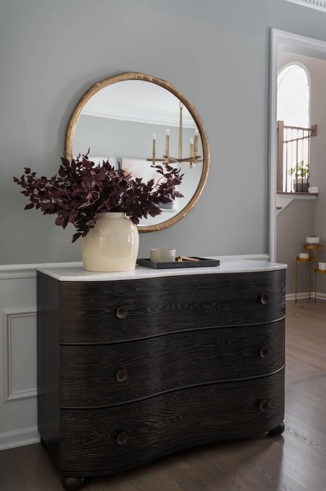 Granger, IN dining room with round mirror, dark wood console, marble top, and vase with burgundy branches