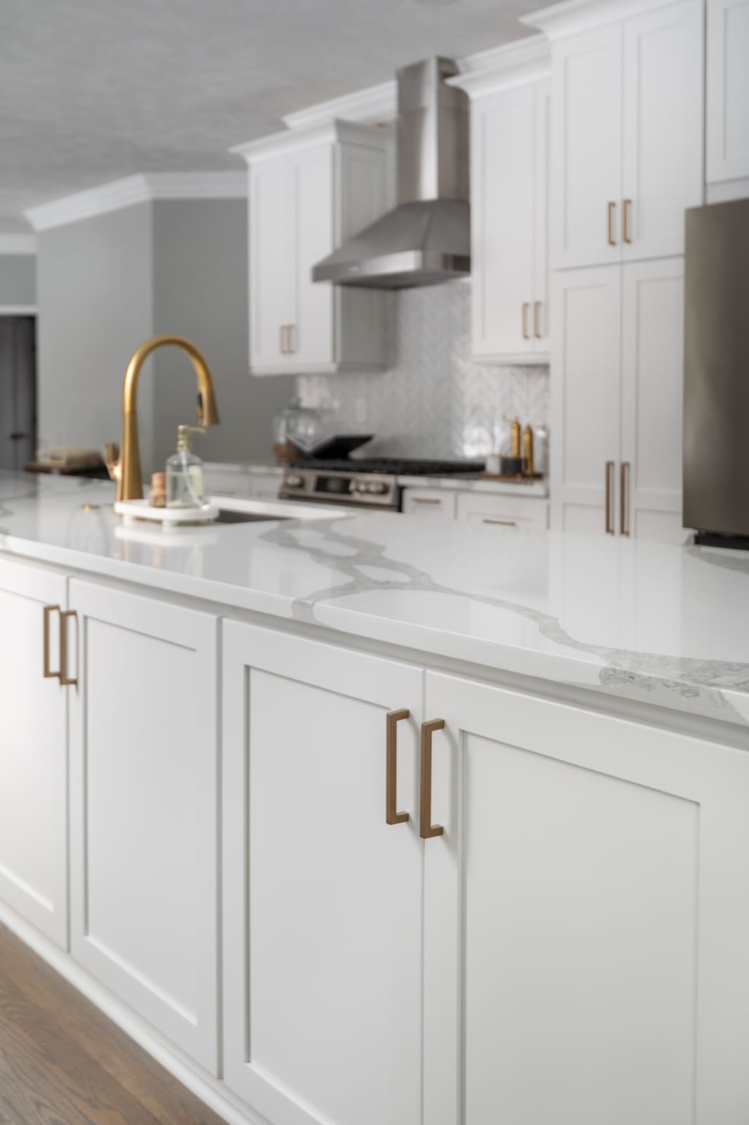 Granger, IN kitchen island with white cabinetry, brass hardware, quartz countertop, and brass faucet