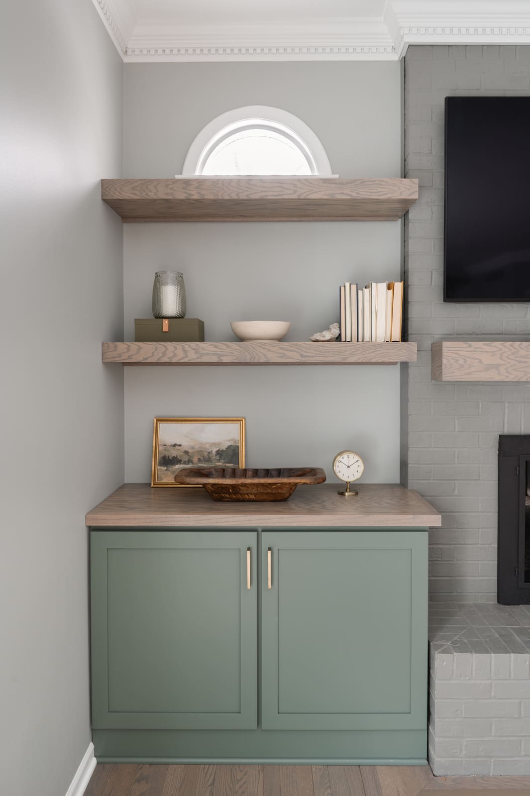 Granger, IN living room built-in with sage green cabinet, wood shelves, art, books, and gray painted brick fireplace