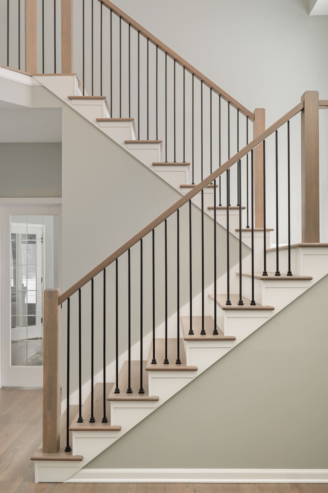 Granger, IN staircase with light wood handrails, black balusters, and tall walls in a bright entry hall