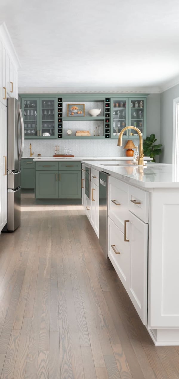 Long view of a Granger, IN kitchen with white cabinets, brass faucet, wood floors, and sage green bar in back