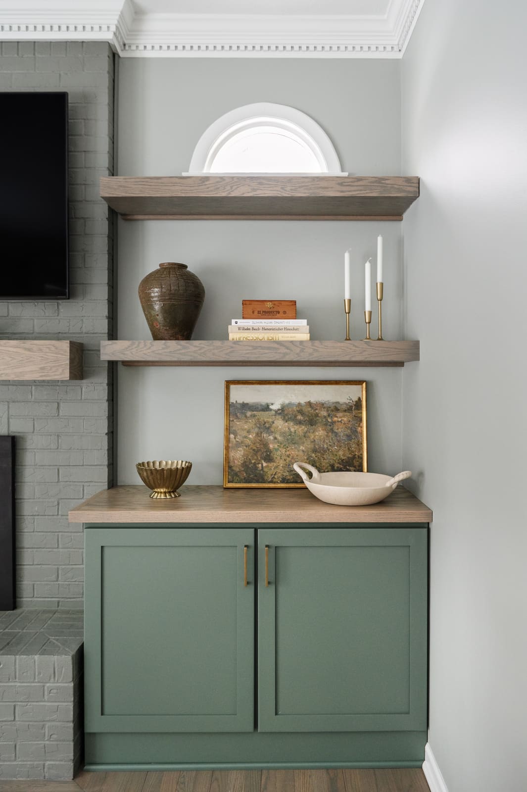 Sage green built-in cabinet in Granger, IN with wood shelves, framed art, pottery, and brass candlesticks
