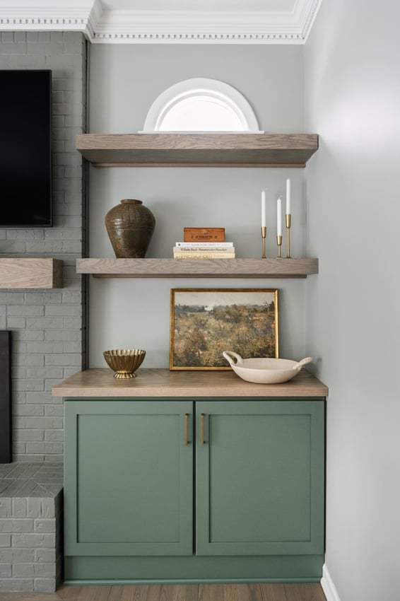 Sage green built-in cabinet in Granger, IN with wood shelves, framed art, pottery, and brass candlesticks