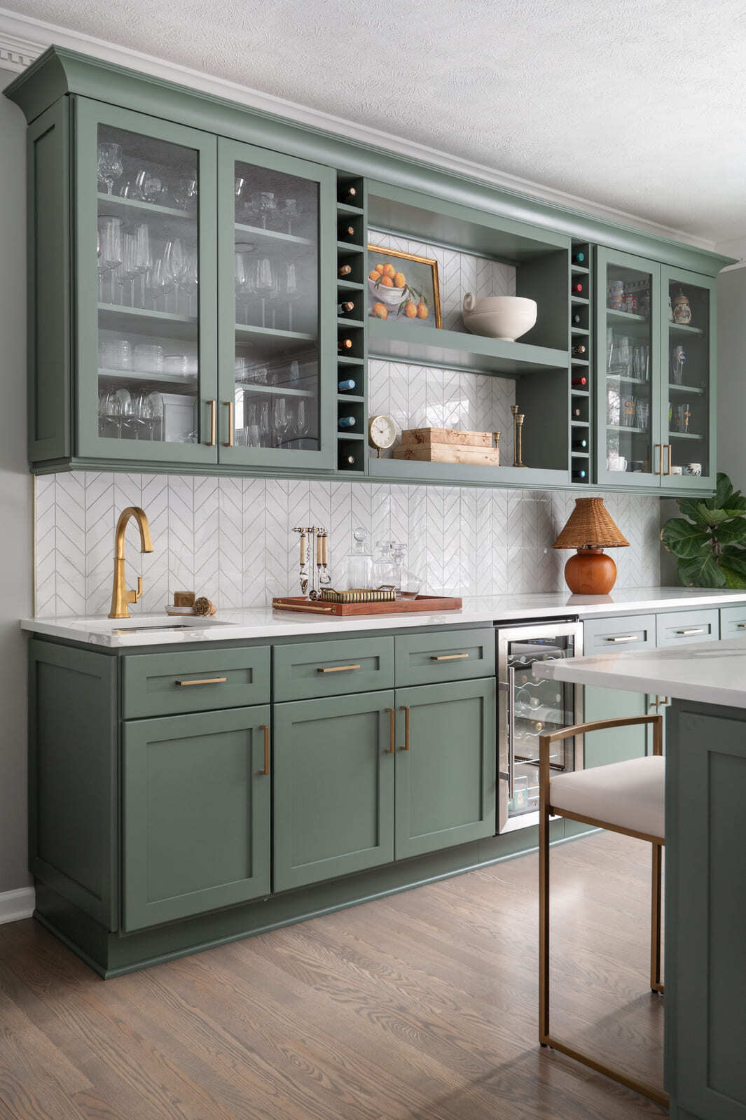 Sage green kitchen cabinetry with glass fronts, wine fridge, and brass faucet in a Granger, IN home