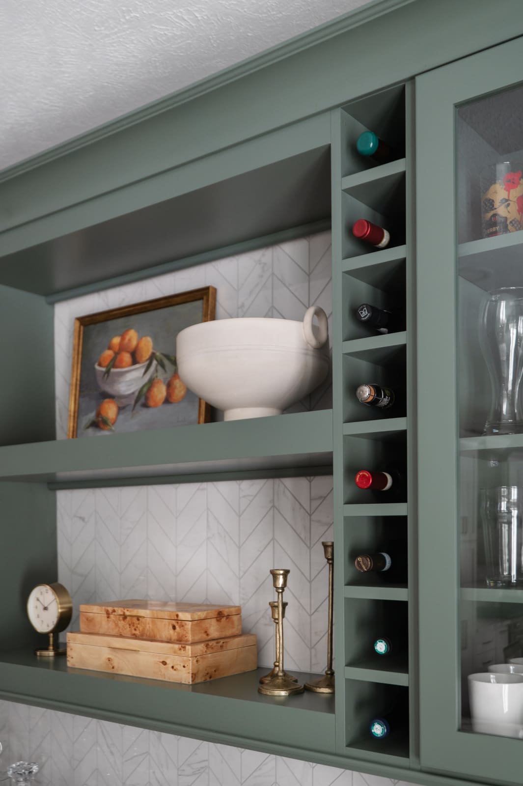 Sage green kitchen cabinetry with wine fridge, open shelves, and white chevron tile backsplash in Granger, IN