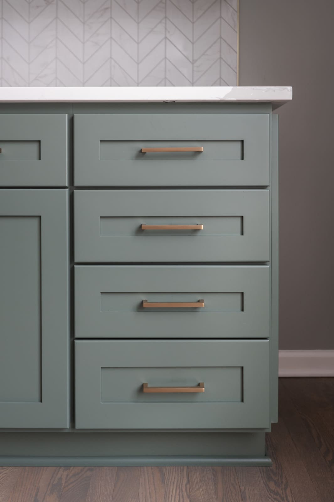 Sage green kitchen drawers with brass pulls and white quartz countertop against chevron tile backsplash in Granger, IN