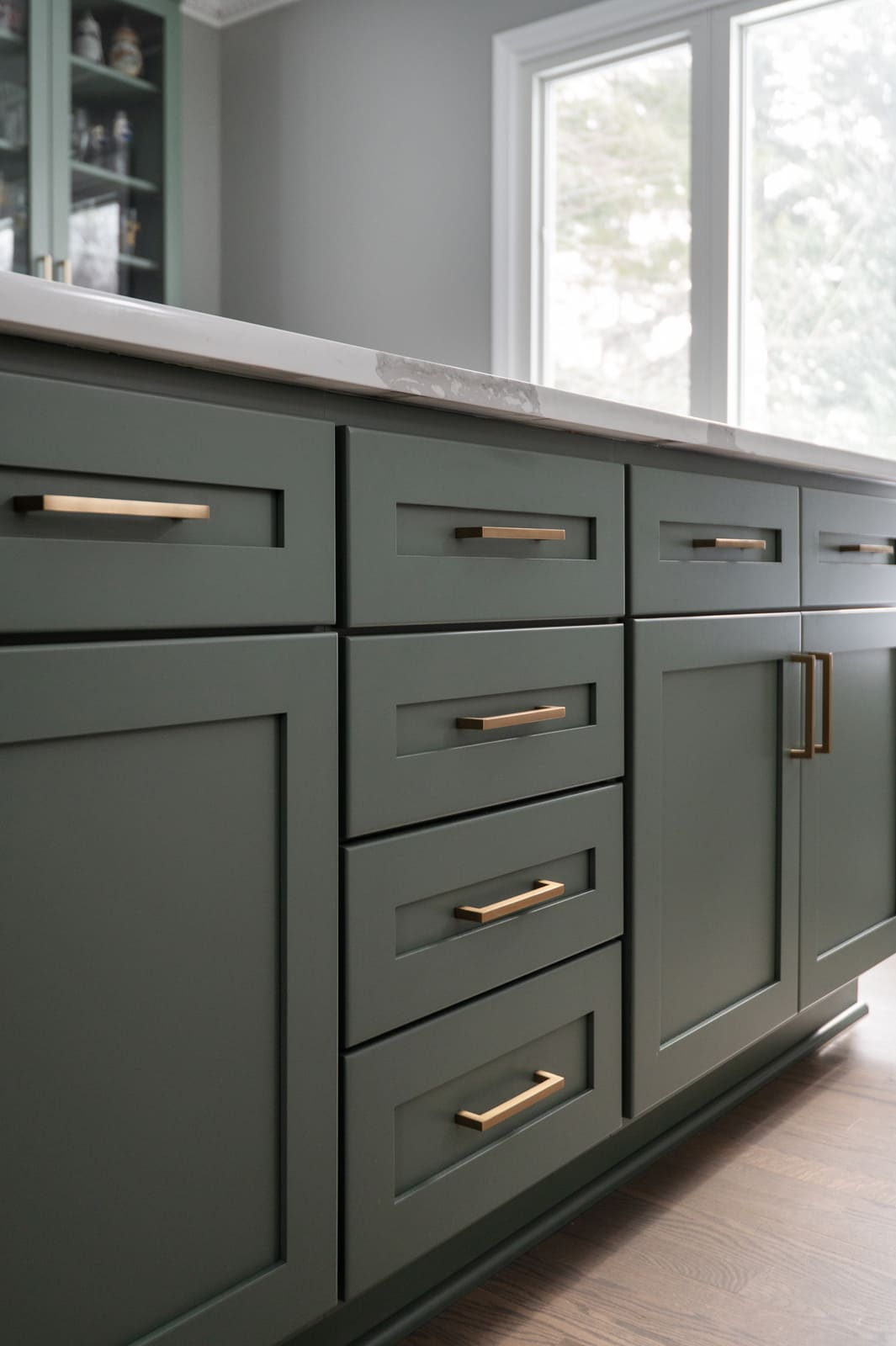 Sage green kitchen island drawers and cabinets with brass hardware and white quartz countertop in Granger, IN