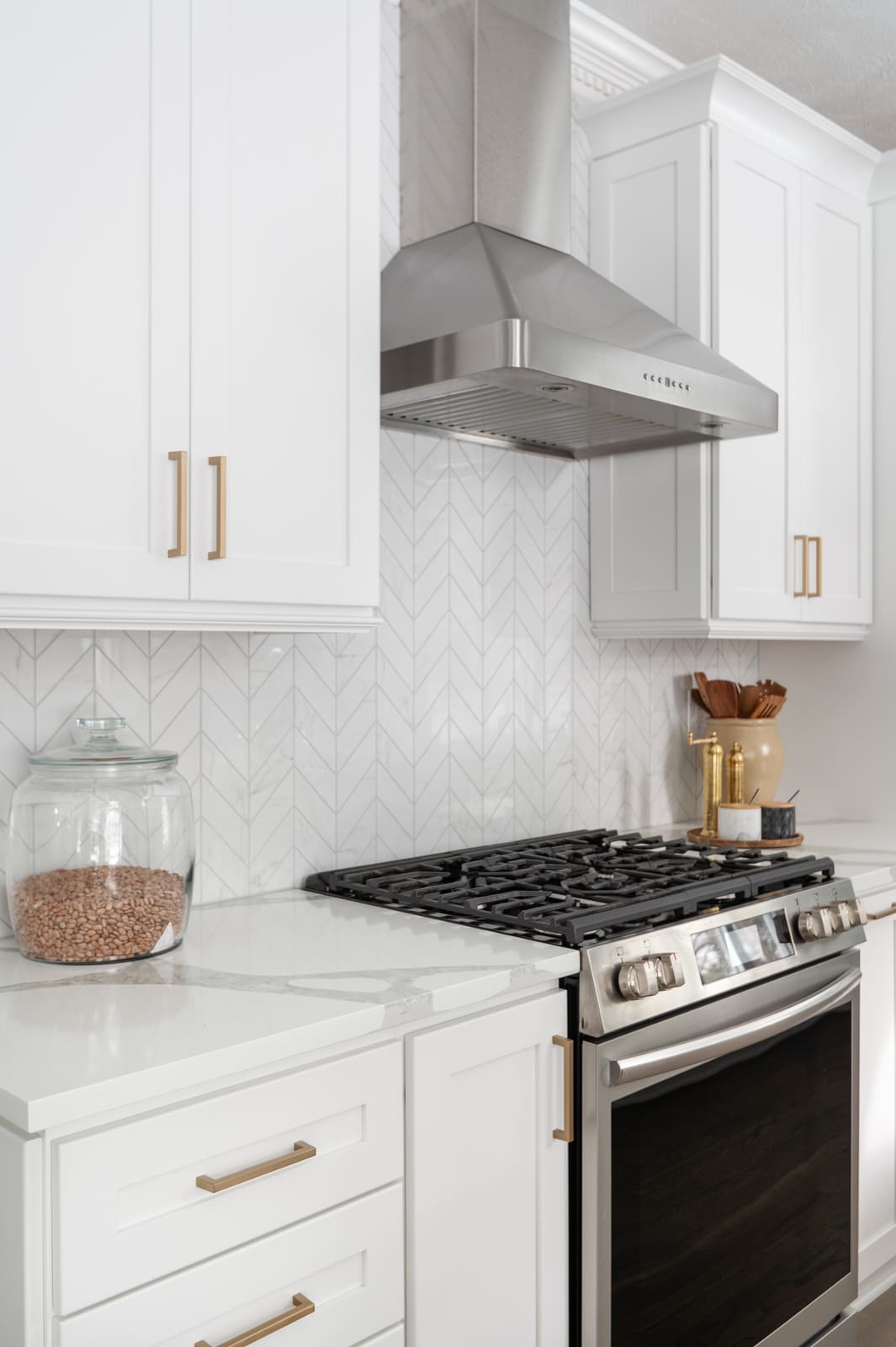 Stainless range and hood with white cabinetry, brass hardware, and chevron tile backsplash in Granger, IN kitchen