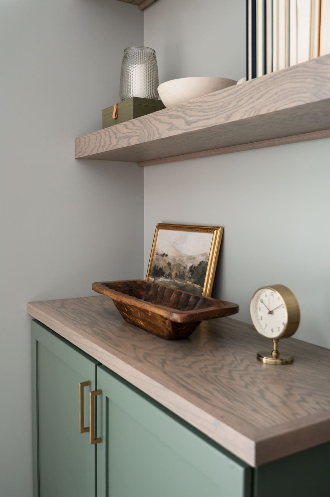 Styled sage green built-in in Granger, IN with wood countertop, clock, framed art, and decorative tray