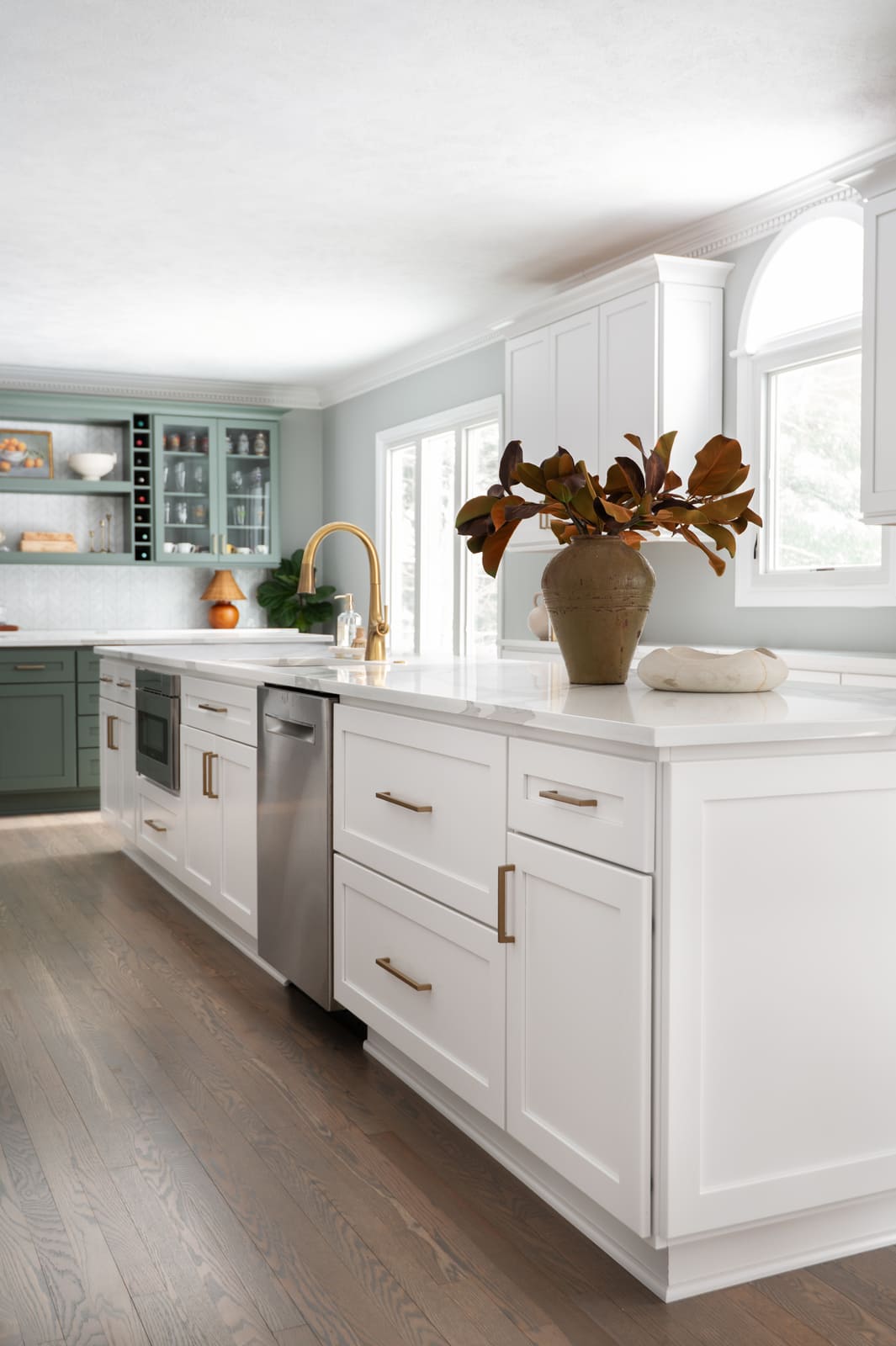 White kitchen in Granger, IN with long island, brass faucet, stainless appliances, and sage green bar in the background