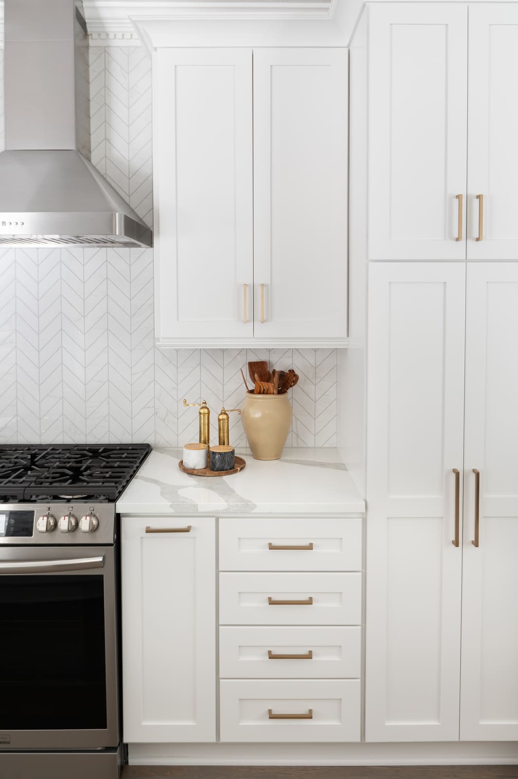 White kitchen range wall with stainless hood, brass hardware, and white chevron tile backsplash in Granger, IN