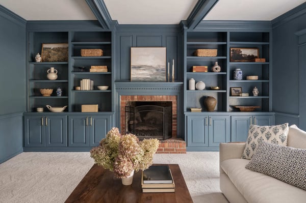 Blue living room with built-in shelves, brick fireplace, white sofa, wood coffee table, and coffered ceiling.