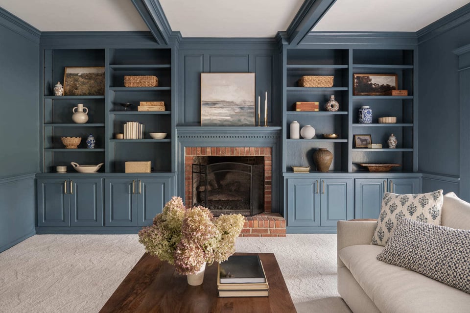 Blue living room with built-in shelves, brick fireplace, white sofa, wood coffee table, and coffered ceiling.