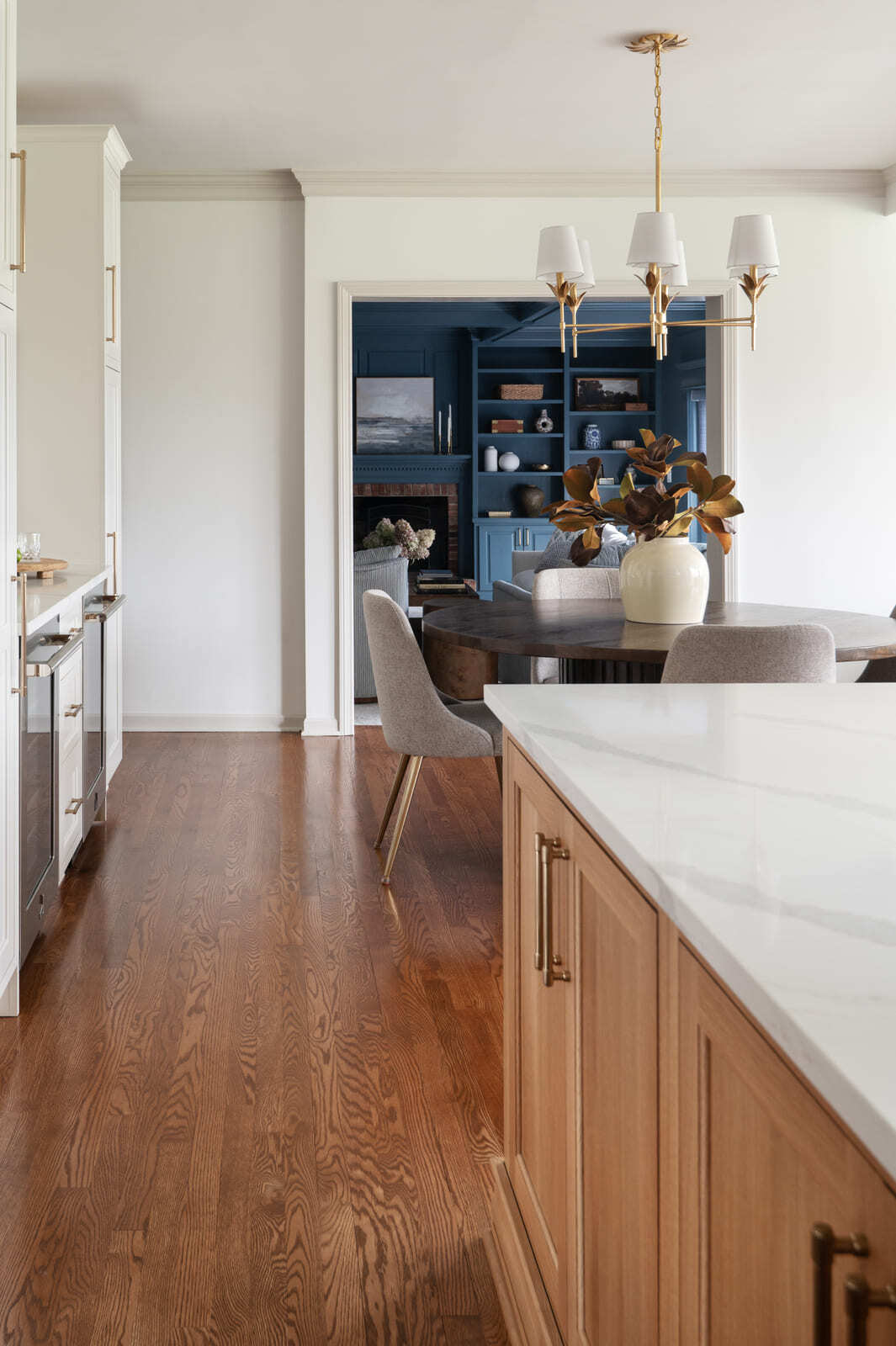 Bright kitchen and dining area with wood island, round table, brass chandelier, and view into blue living room.