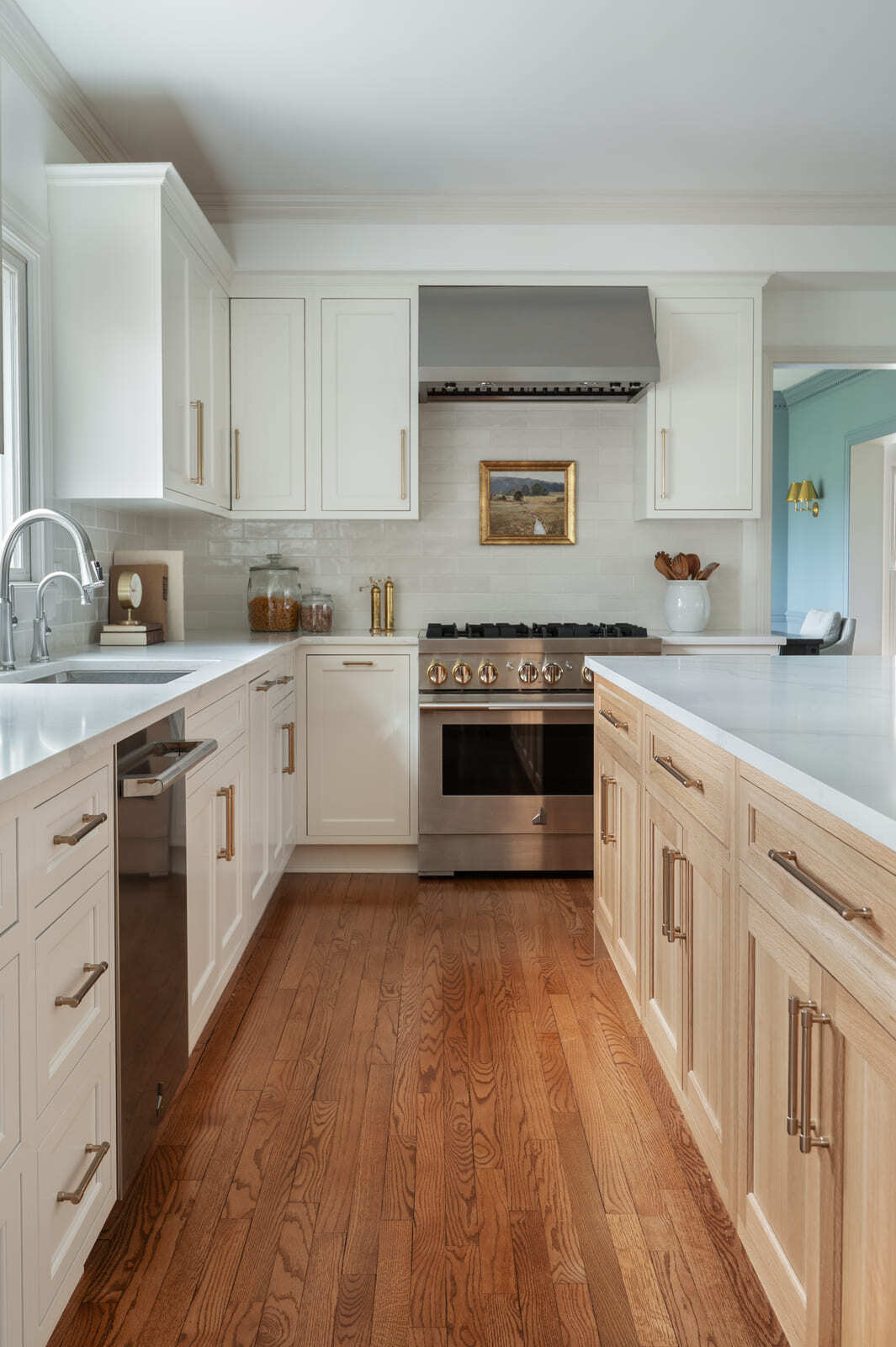 Bright kitchen with white cabinets, wood island, brass pulls, stainless range, tile backsplash, and wood floors.
