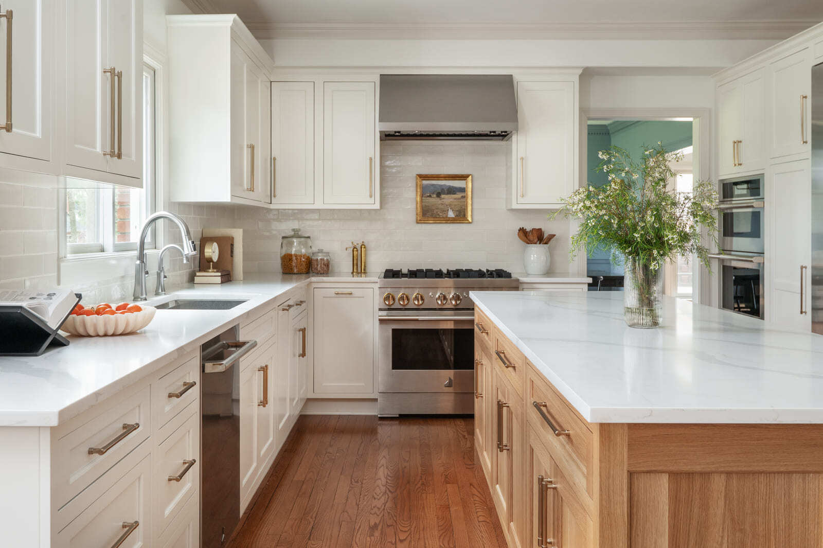 Bright white kitchen with wood island, brass hardware, stainless range, large island, and warm wood floors.