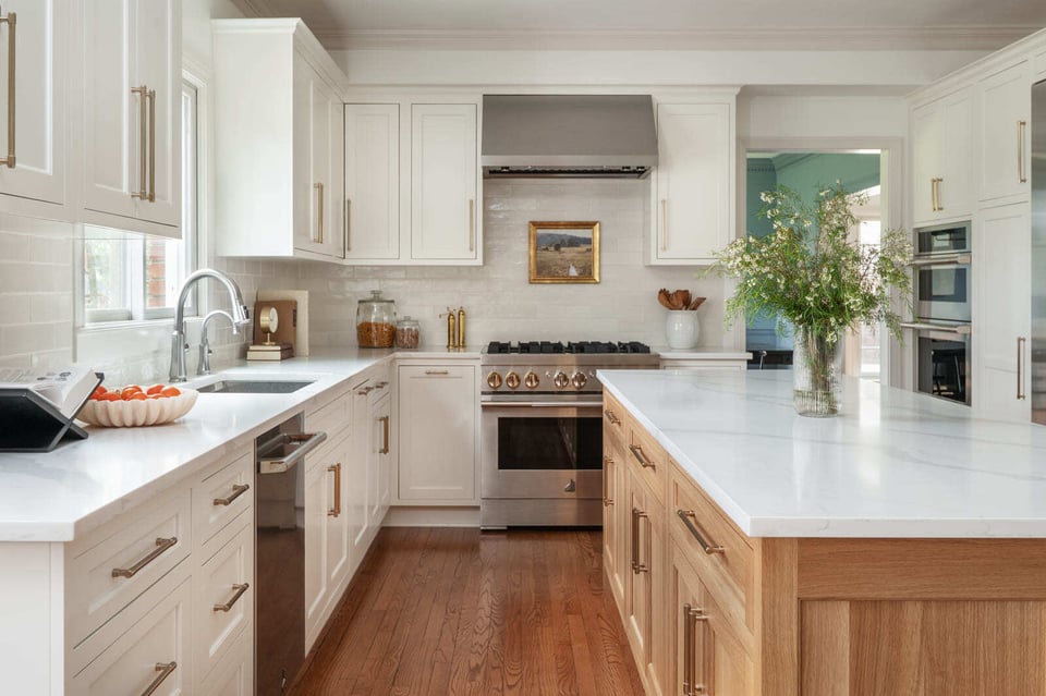 Bright white kitchen with wood island, brass hardware, stainless range, large island, and warm wood floors.