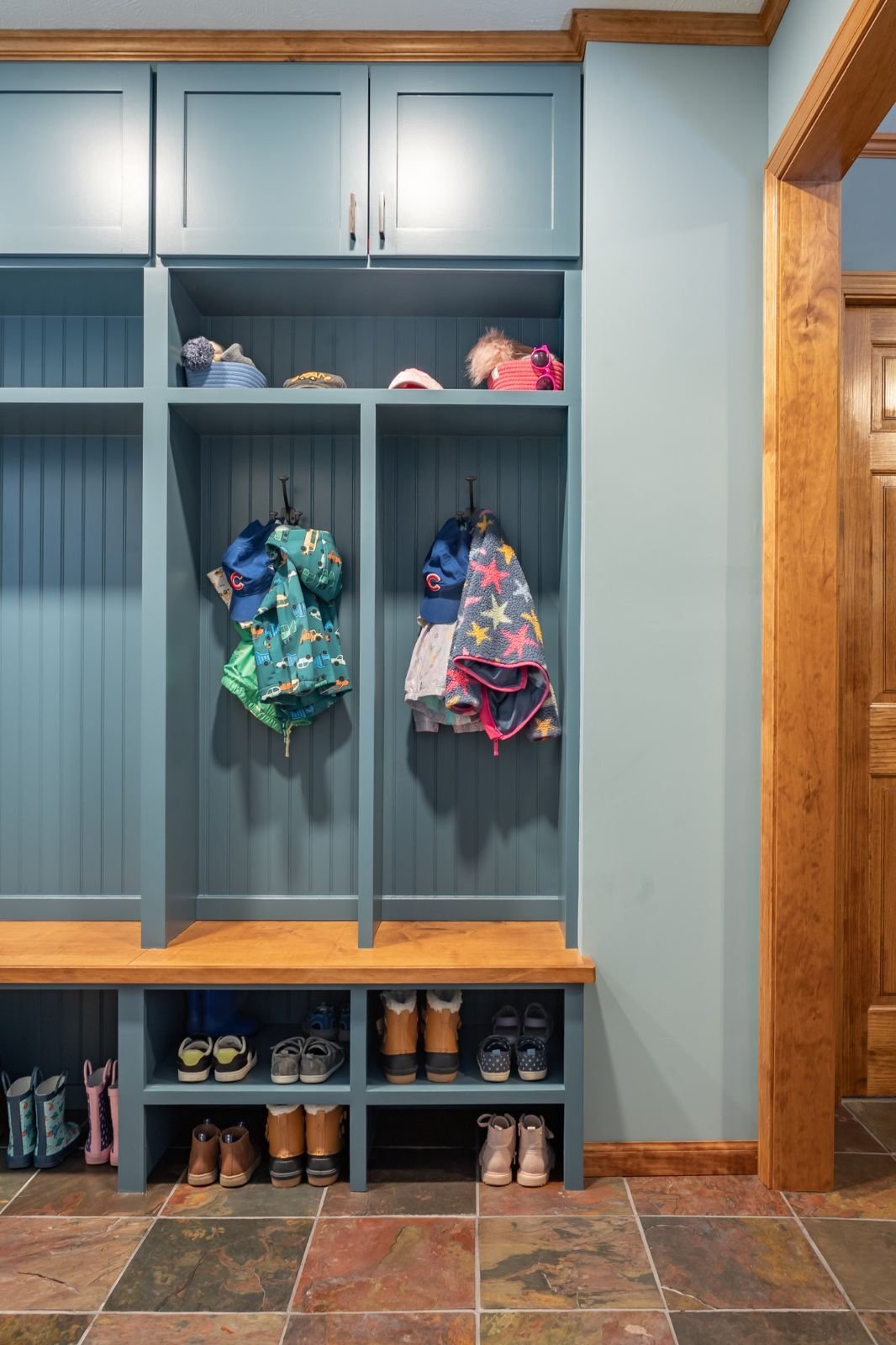 Blue mudroom storage with wood accents and hooks for coats and hats located in Indiana