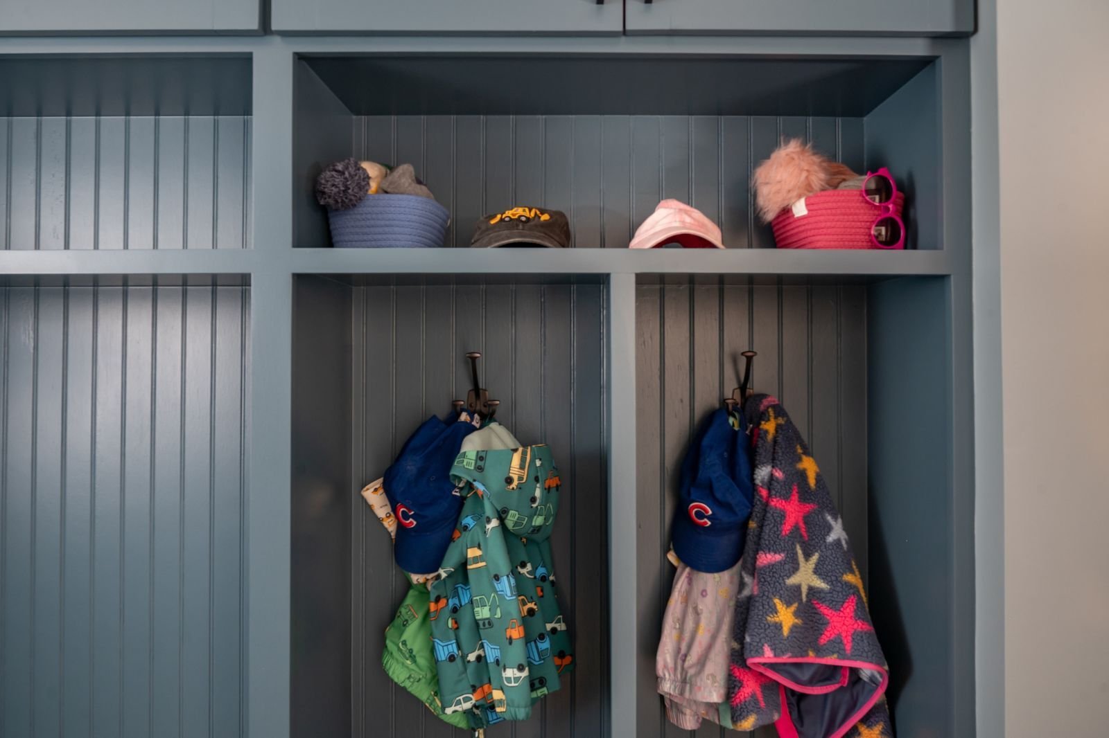 Detail of blue mudroom cubbies with hats and children’s jackets hanging on hooks located in Granger, IN