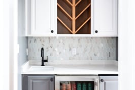 Indiana wet bar with glass-front beverage fridge, chevron wine rack, white cabinetry, modern backsplash, and statement chandelier