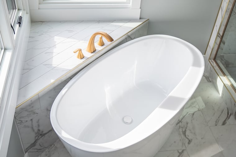 Porcelain tub with brass faucet fixtures near window in bathroom remodel by Peacock and Co.