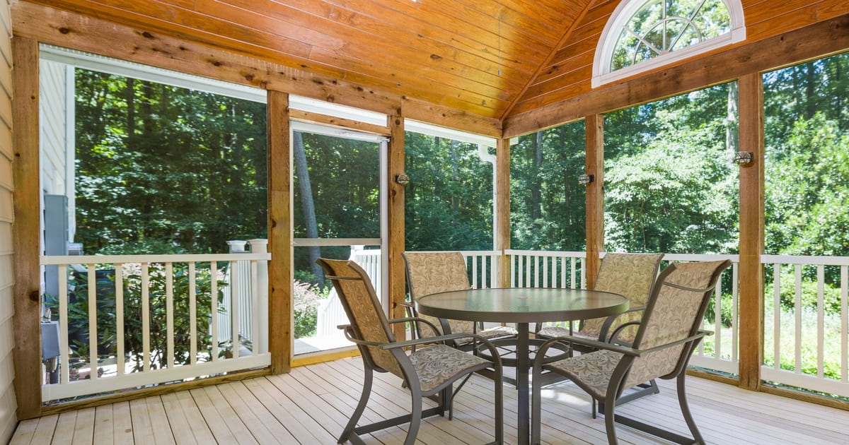 Screened porch interior with wood framework on sunny day with patio table and four chairs