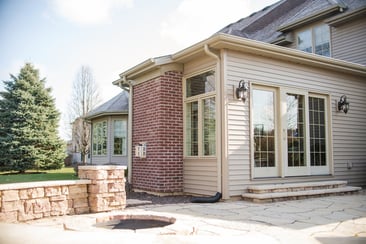 Sunroom addition exterior with patio and fire pit next to seating wall