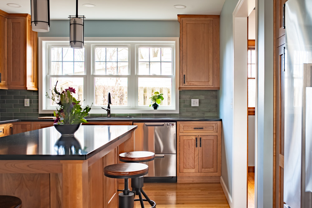 Wide view of kitchen remodel with cherry shaker cabinets, black quartz countertops and large kitchen window by Peacock & Co in South Bend